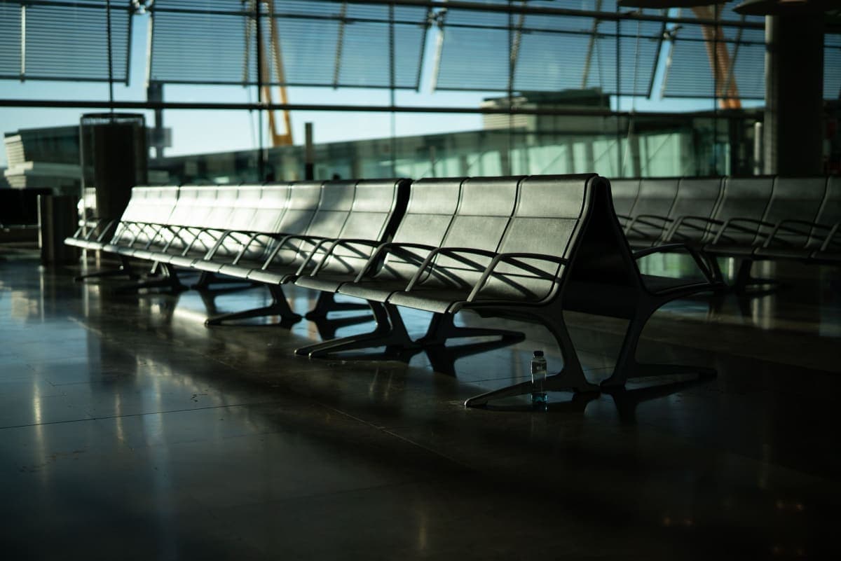 A quiet, empty airport seating area with sunlight coming through tall terminal windows