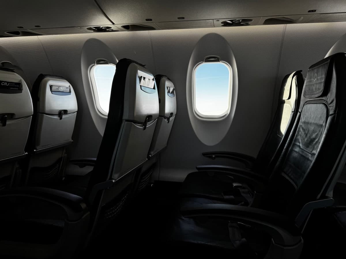 The interior of an empty aircraft cabin with bright sky visible through the window