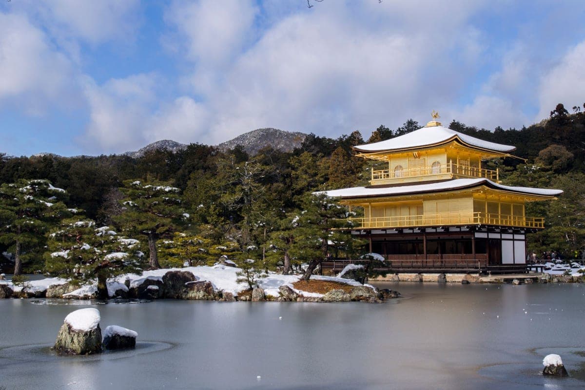 Kinkaku-ji, the Golden Pavilion in Kyoto, with snow on its roofs and a frozen pond under a blue winter sky