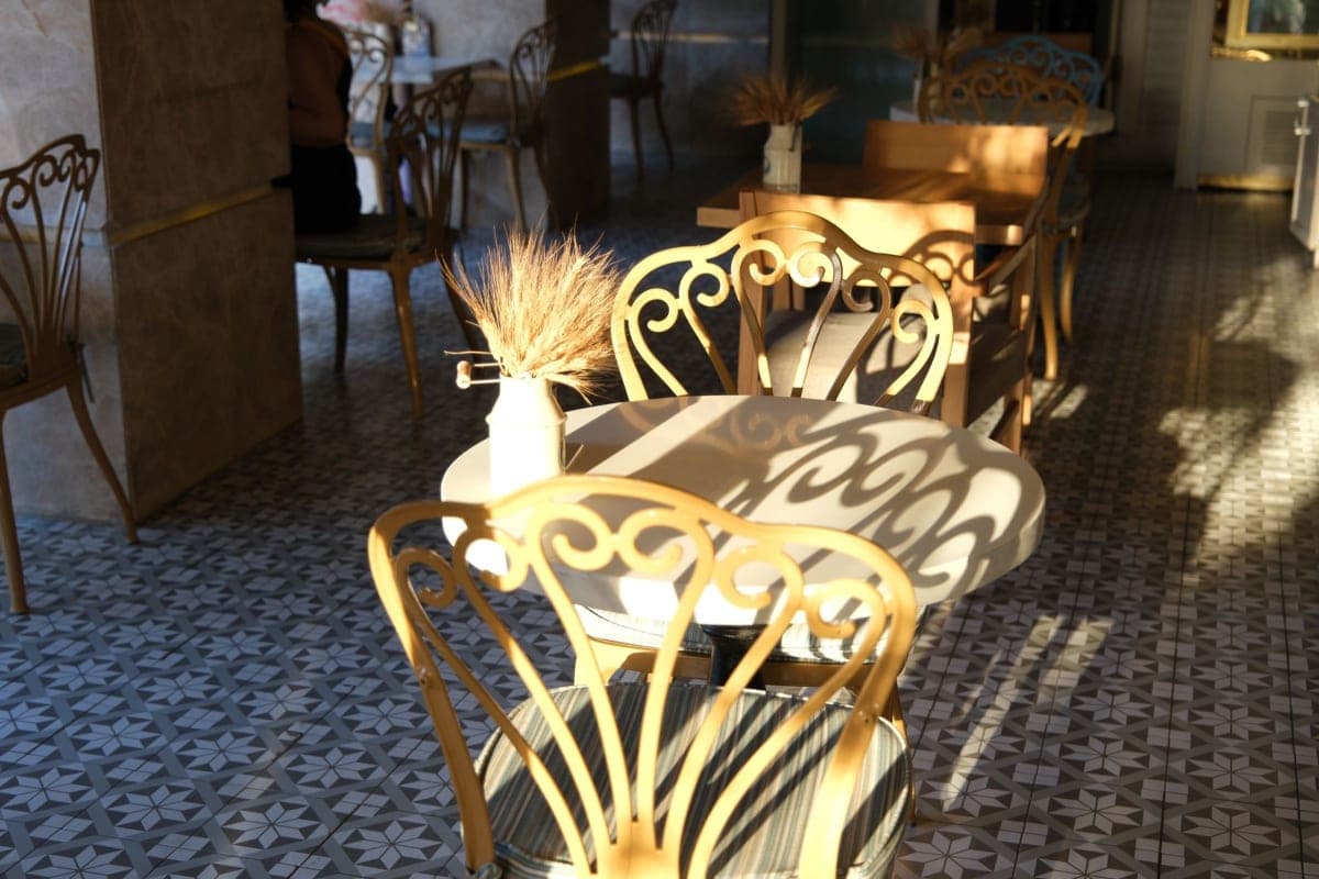 Un rincón tranquilo e iluminado de un café con sillas de hierro forjado y suelo de baldosas estampadas