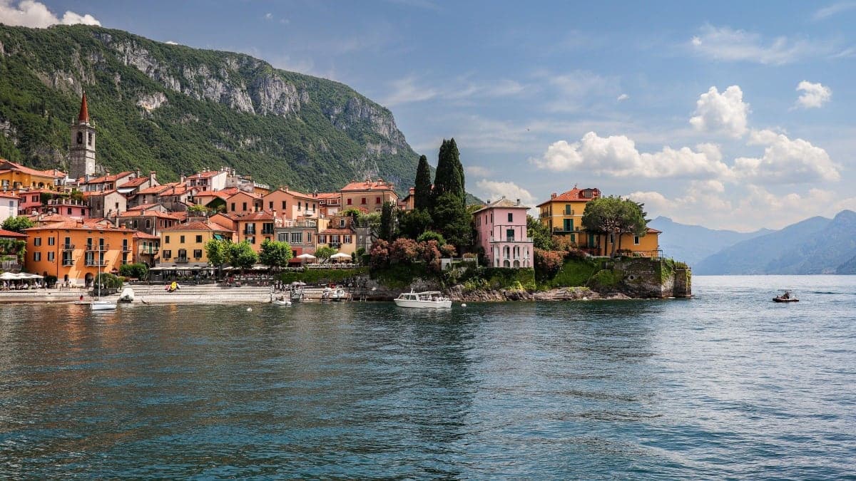 Varenna's colourful lakeside houses and bell tower below green mountains on Lake Como, Italy