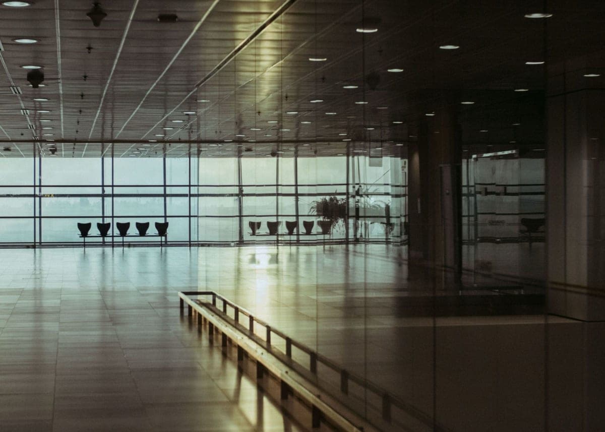 The interior of an airport terminal in daylight, empty seating and tall windows, no signage visible