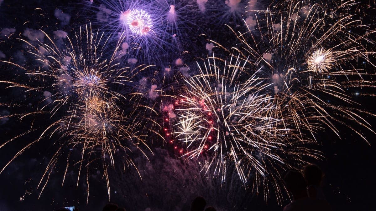 Fireworks bursting over a dark sky above a silhouetted New Year's Eve crowd