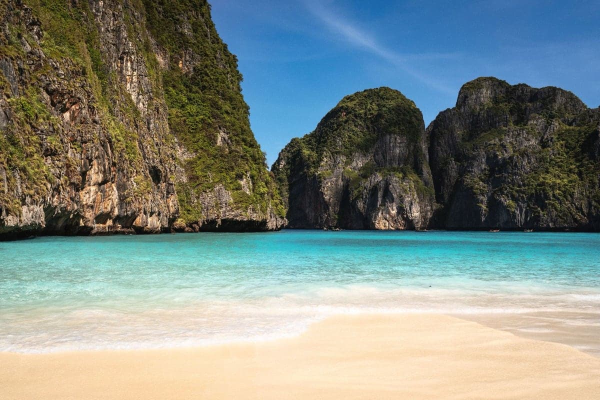 A longtail boat moored in shallow turquoise water beside limestone cliffs in southern Thailand
