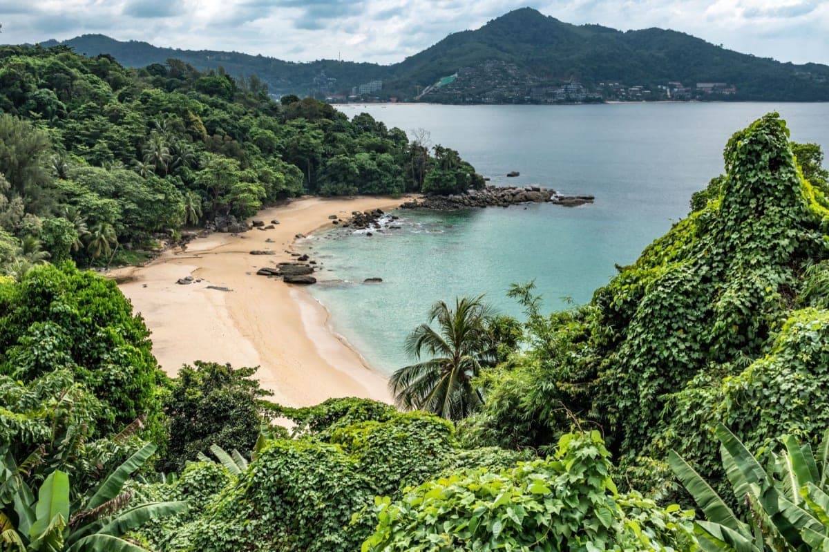 A sheltered beach cove in Phuket, Thailand, with turquoise water and green hills